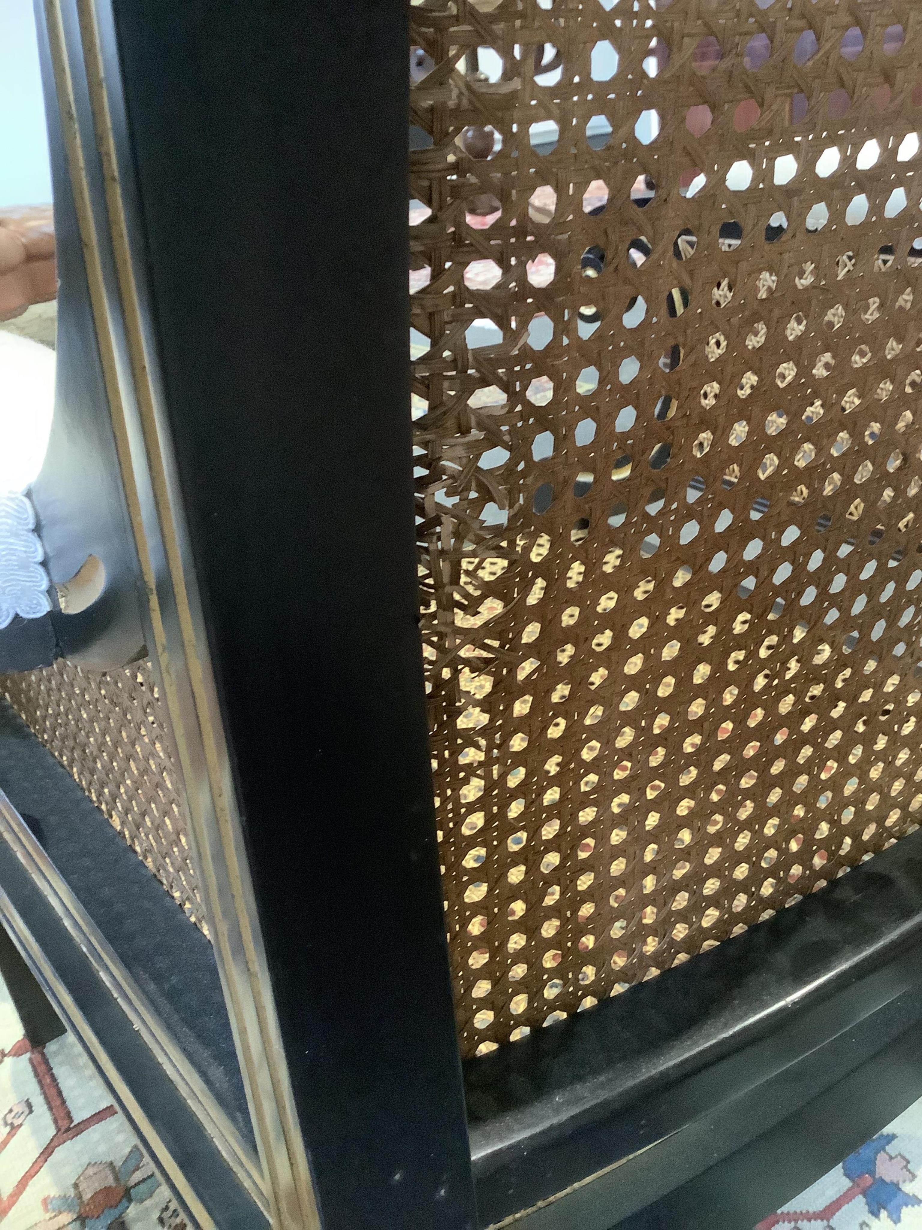 A pair of Regency style ebonised, parcel gilt caned bergere elbow chairs